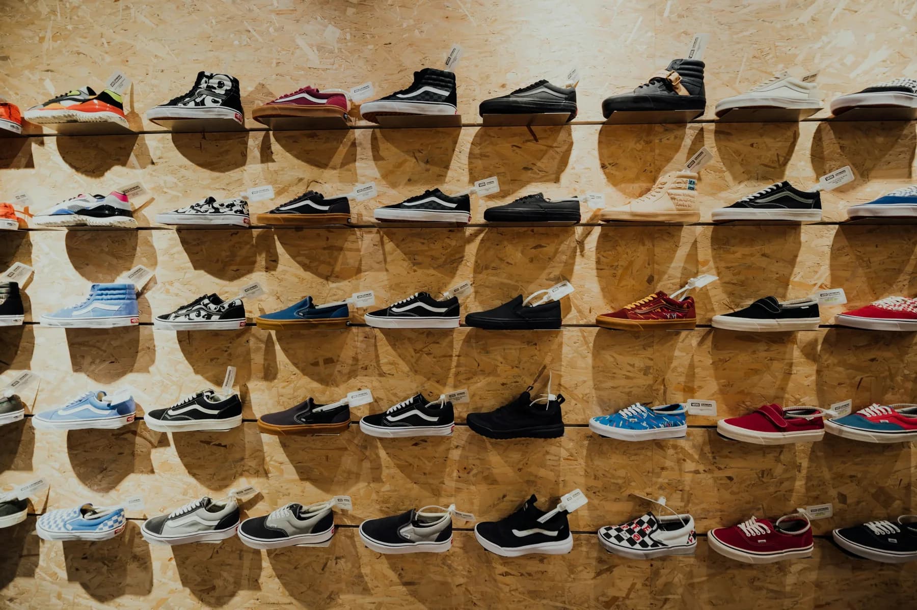 Five shelves of Vans sneakers mounted on a plywood store wall, each pair tagged and displayed in profile